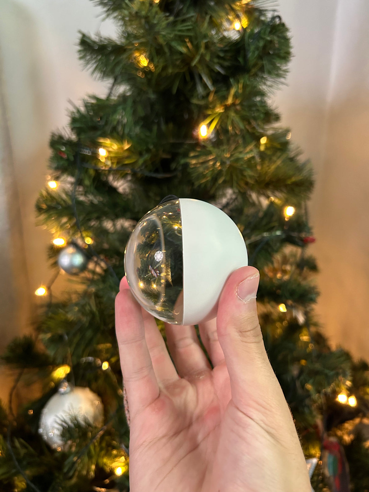 Memory Orb in white, held in front of a Christmas tree – clear dome with the screen inside